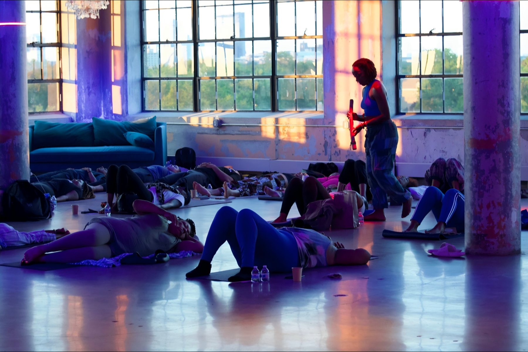 Participants lying on mats in a loft bathed in violet and blue light while Andrea stands and guides the room