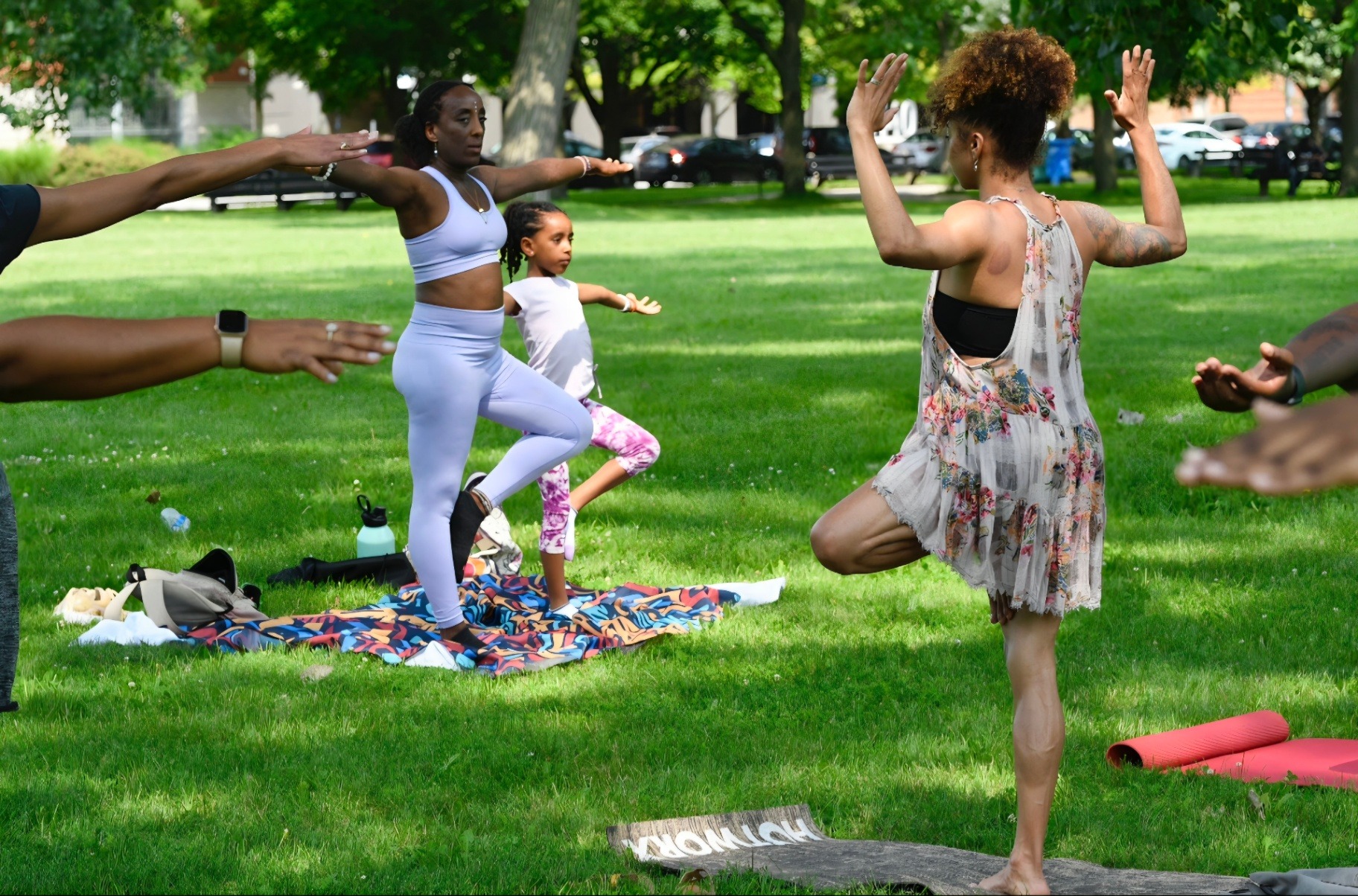 Andrea guiding tree pose with Ava and neighbors during an outdoor yoga gathering in the park